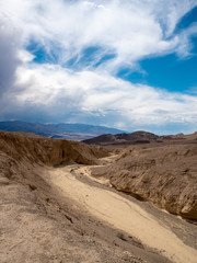Fototapeta na wymiar Water erosion formed wash (ravine) and approaching rain storm in Death Valley National Park, vertical orientation.