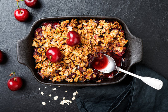 Cherry crumble in black baking dish on black stone background. 