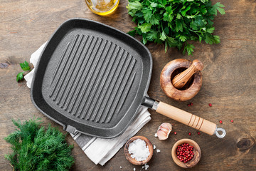 Empty cast-iron grill pan with ingredients for cooking on wooden background, top view 