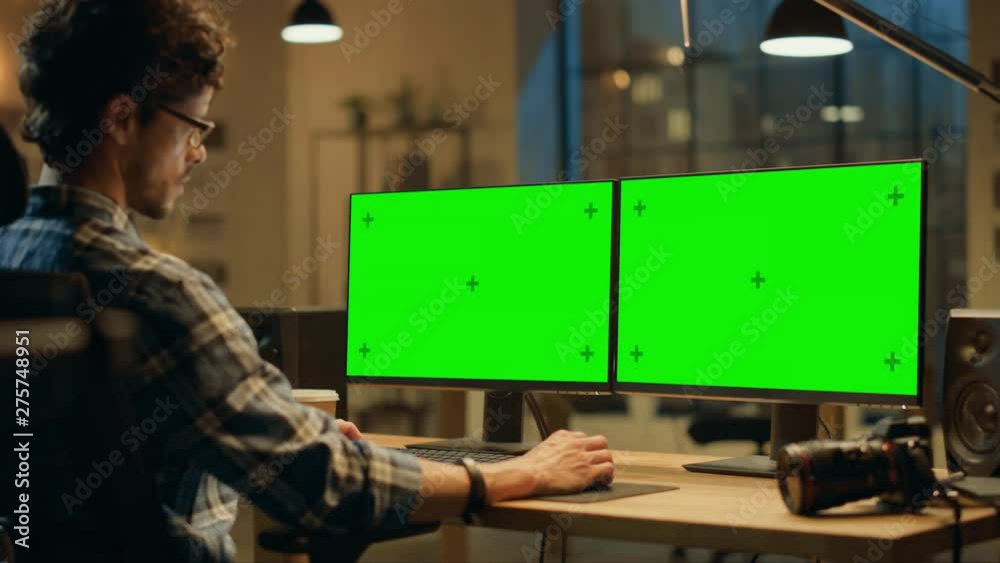 Aufkleber over the shoulder: creative designer sitting at his desk uses desktop computer with two green mock-u