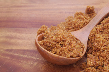 Dark brown sugar and wooden spoon on wooden background 