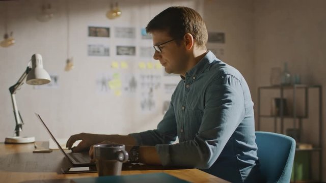 Professional Creative Man Sitting at His Desk in Home Office Studio Working on a Laptop. Man working with Data and Analyzing Statistics. Camera Moving Around. 360 Degree Tracking Arc Shot Movement