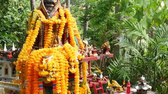 Wooden miniature guardian spirit house. Small buddhist temple shrine, colorful flower garlands. San phra phum erected to bring fortune. Traditional respect animistic rituals, pray ceremonies