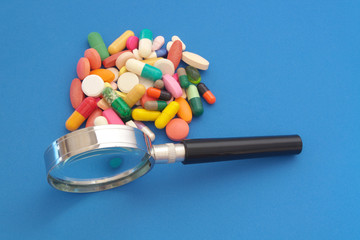 Review drugs concept, many pills and drugs with magnifying glass on blue background