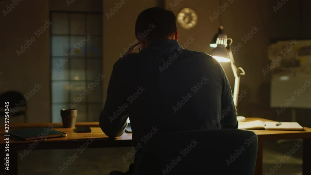 Poster Professional Creative Man Sitting at His Desk in Office Studio Working on a Laptop in the Evening. Man working with Data and Analyzing Statistics. 360 Degree Tracking Arc Shot Movement
