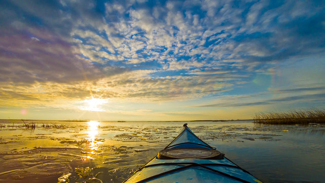 View from bow (prow) of blue kayak on lake with ice floes in winter or early spring at buatiful sunset. Winter kayaking