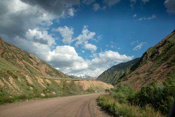 Fototapeta premium The car on the road between the hills with snow-capped mountains on the horizon. Travel, Kyrgyzstan