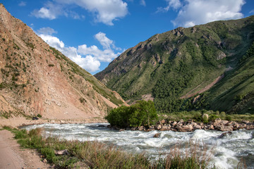 Fototapeta na wymiar River flowing between green hills with snow-capped mountain peaks on the horizon against a cloudy sky