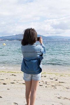 Girl taking picture with the mobile phone of the beach and the sea