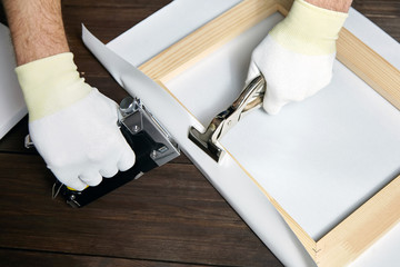 Canvas stretching. Wooden stretcher bar, staple gun, canvas pliers, male hand in white protect glove