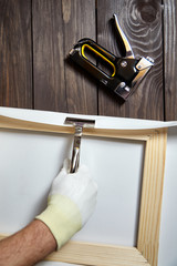 Canvas stretching. Wooden stretcher bar, staple gun, canvas pliers, male hand in white protect glove