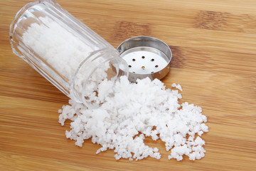 Glass salt shaker on wooden table and organic sea salt