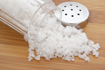 Glass salt shaker on wooden table and organic sea salt 