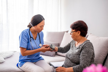 Asian Caregiver measuring blood pressure of senior woman at home. Kind carer measuring the blood pressure of a happy elderly woman in bed in the nursing home.