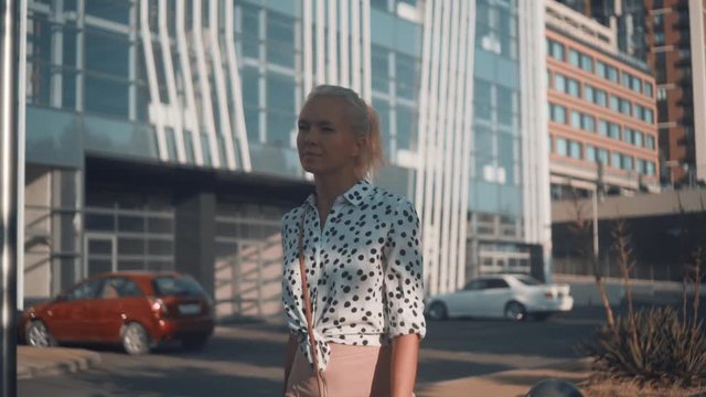Caucasian young business woman in a white shirt with black peas walking down the street near a modern office building. The average plan.