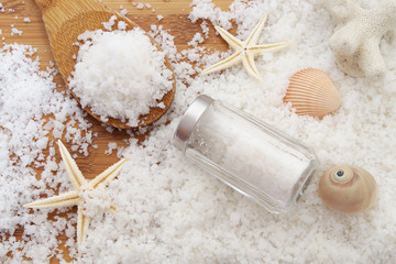 Sea salt concept. Salt on wooden background with spoon and salt shaker and starfish with seashells
