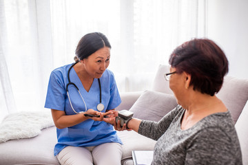 Friendly young female doctor examining elderly woman. Home care nurse measuring blood pressure of senior woman. Medical care, insurance, prescription, paper work or career concept.