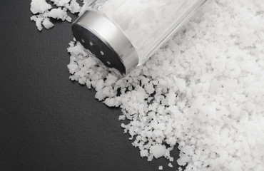 Salt shaker and sea salt on black background
