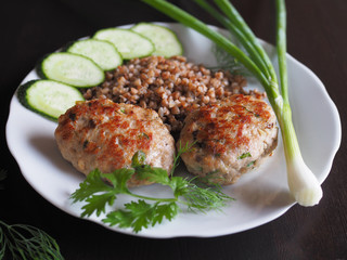  Cutlets with vegetables and garnish are in a white plate on a dark table. 