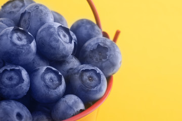 Freshly picked delicious blueberries in a red bucket on a yellow background, detox vegetarian food, close-up image