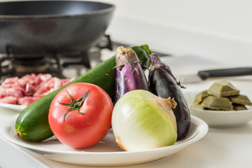 キッチンに夏野菜とお肉とカレールーにフライパンが背景に写っている家庭料理