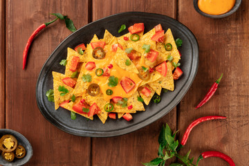 Nachos, Mexican tortilla chips, shot from above with a cheese sauce, chili and jalapeno peppers, tomatoes. and cilantro, on a dark rustic wooden background