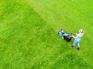 Obraz na płótnie Canvas Beautiful girl cuts the lawn. Mowing lawns. Aerial view beautiful woman lawn mower on green grass. Mower grass equipment. Mowing gardener care work tool. Close up view. Aerial lawn mowing