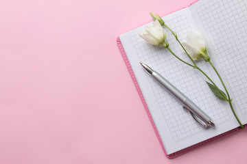 Open pink notebook and white flowers on a bright trendy pink background. top view. office tools