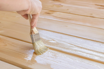 Applying varnish paint on a wooden surface. Man hand with a brush closeup. Painting wood wall and ...