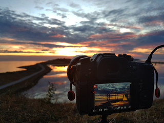 Camera filming and taking pictures of a colordull sunset at the ocean.