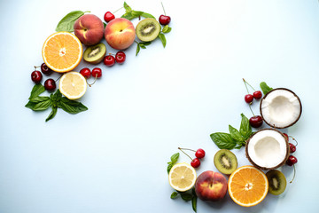 Creative layout made of summer fruits. Food concept. Peach, kiwi, lemon, cherries, oranges and coconut on light blue background