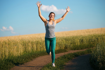Happy woman on sunset or sunrise. Female runner raising arms expressing positivity and success.
