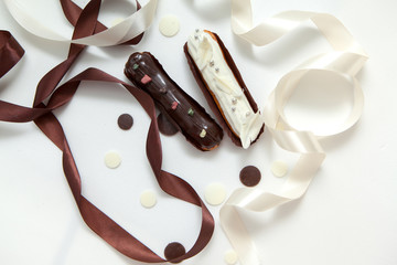 Close-up of a set of two eclairs with different fillings and design isolate on a white surface decorated with chocolate drops, white and brown silk ribbon