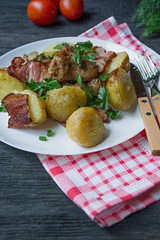 Baked young potatoes with meat and vegetables. Dark wooden background.