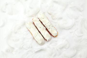 A set of three eclairs with white chocolate decor isolate on a white surface decorated with white feathers