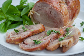 Baked pork roll with greens served on a white plate. Light background.