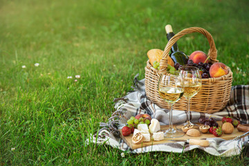 Picnic setting with  two glasses of white wine,  cheese, fruits and basket. Outdoor, green lawn