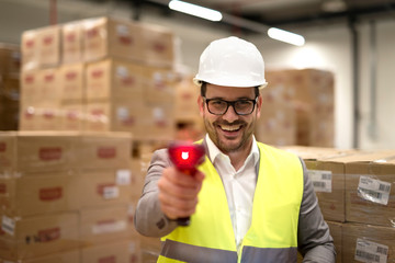 Portrait of factory warehouse worker standing among cardboard boxes holding bar code scanner laser...