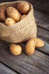 Raw potato food . Fresh potatoes in an old sack on wooden background
