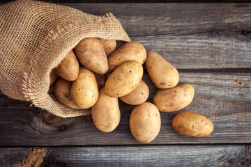 Raw potato food . Fresh potatoes in an old sack on wooden background