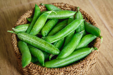 The crop of peas lies in a round wicker basket on a wooden background. Close up.
