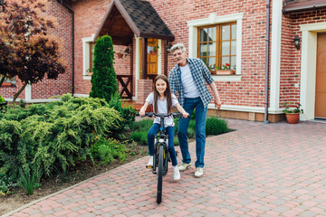 First lessons cycling riding. Handsome grandather teach his granddaughter against.