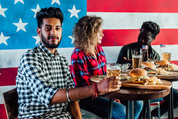 Group of millennial friends spending quality time together at restaurant eating hamburgers and beer.