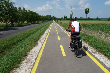 Female cyclist with pannier bags and helmet on tour. Rear view of backpackers riding a bicycle in the new cycle path. Sports and cycling,healthy lifestyle, traveling on bikes concept.