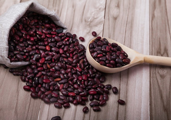 red beans scattered out of the bag and a wooden spoon lie on a wooden background