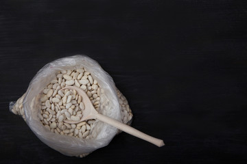 white beans and wooden spoon in a plastic bag on a black background. Trend. Plasicfree