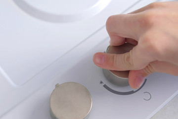 Kid presses the rotary switch with an effort to turn on gas stove. Hand close-up.