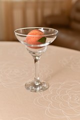 Transparent glass vase with ripe, fresh peach with a leaflet. In the interior of the room, on the table, decorated with a tablecloth, in beige tones. Side view, sveerkha.