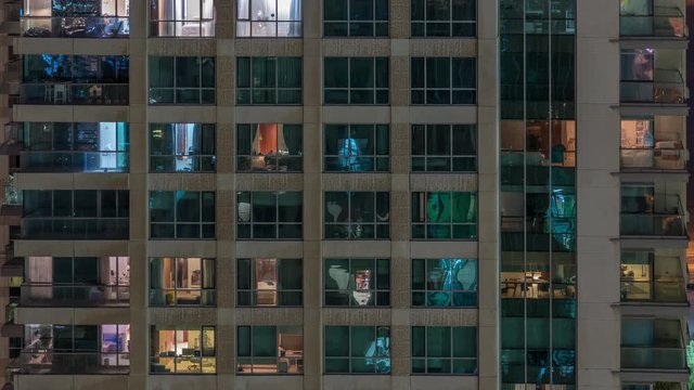 Glowing windows of the multi-storey building with lighting inside and moving people in apartments timelapse. Aerial view of modern residential skyscrapers in Dubai greens district