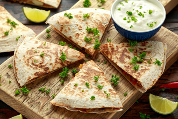 Mexican quesadilla with chicken, corn, black beans, cheese, vegetables, lime and yogurt sauce on wooden board